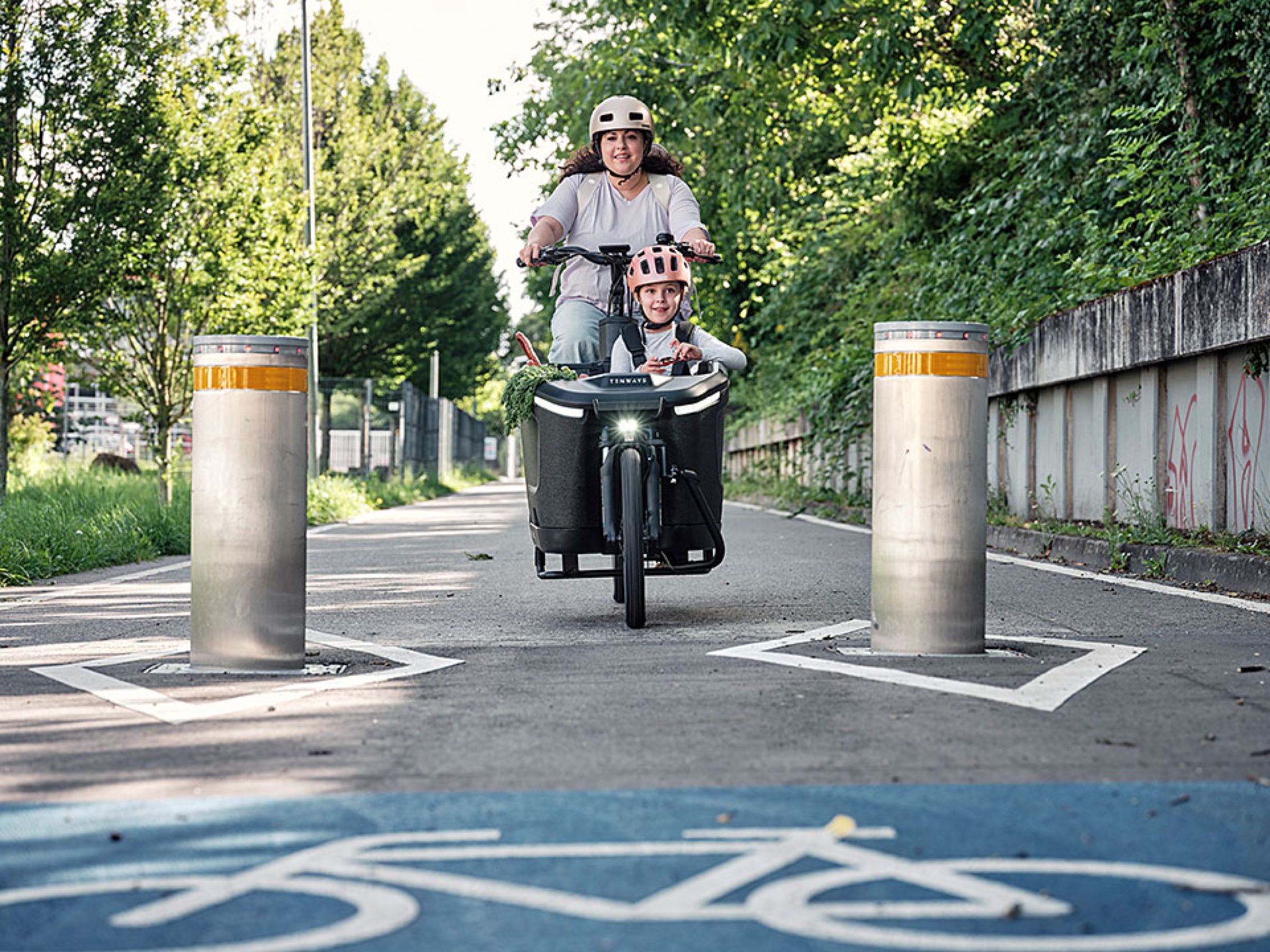 Mama mit Kind im Lastenrad auf Fahrradstraße fährt frontal auf Betrachter zu